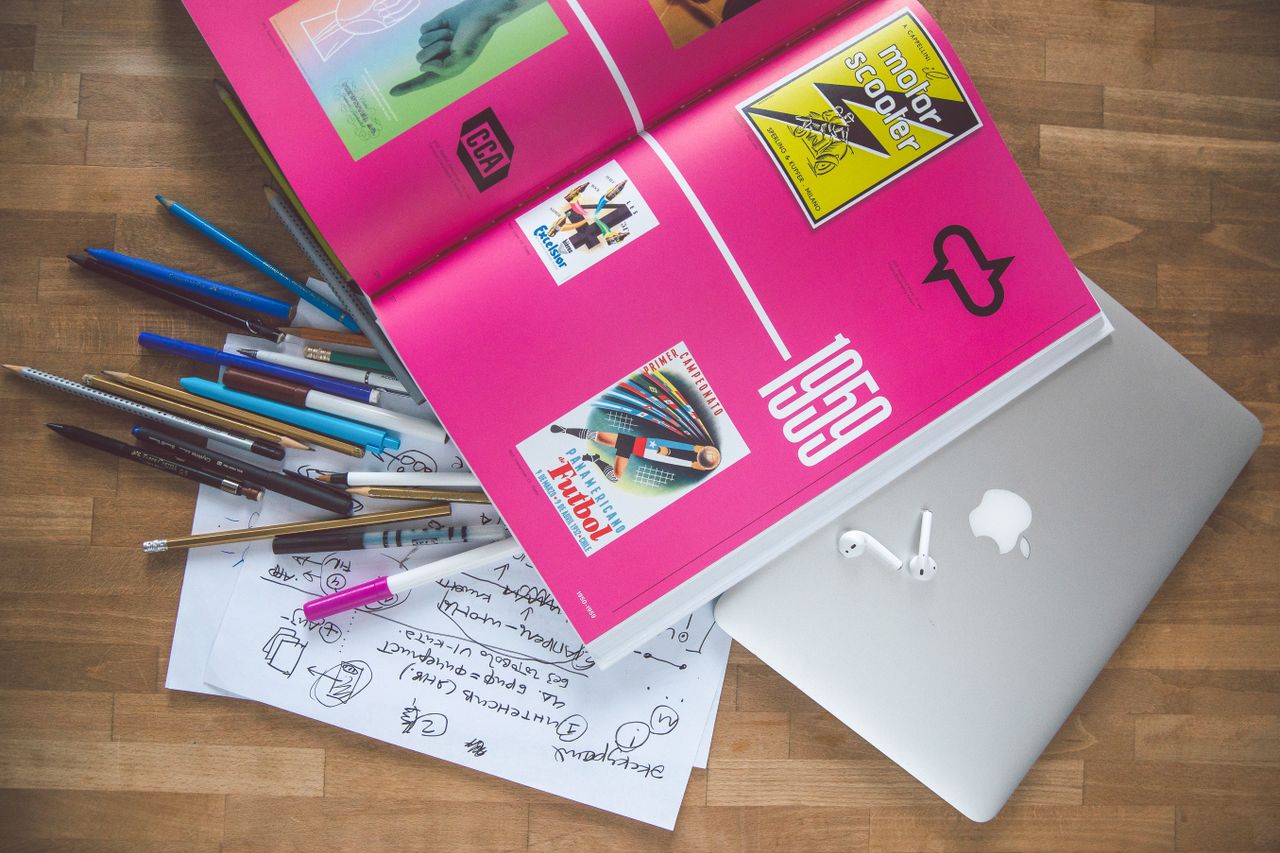 Un bureau lumineux avec un livre de design, un ordinateur portable et des outils créatifs, parfait pour stimuler l’inspiration.